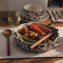 Leaf-pattern ceramic serving bowl holding vegetables, with wooden serving spoon