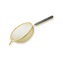 Round fine mesh strainer with gold rim and dark handle, for draining cookware