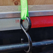 Black S-hook with green webbing attached to a metal trailer rail, ratchet tie-down