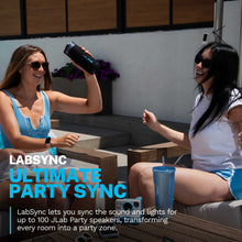 Portable speaker with blue accent logo and textured black body, set on a bench outdoors.