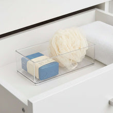 Clear plastic organizer bin with soap bar and loofah, set on a cabinet shelf