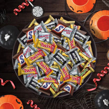 Assorted mini chocolate candy bars in a pile on a dark surface with Halloween decor