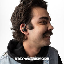 Person wearing a true wireless earbud, black in-ear design with orange skull logo.