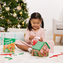 Child holding an icing tool while playing with the wooden gingerbread house set
