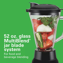 Glass blender jar with black lid and visible fruit and vegetables