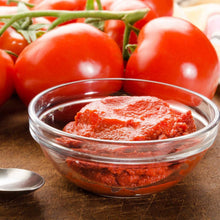 Tomato paste in glass bowl with spoon, with red tomatoes