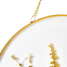 Close-up of round gold-rim glass wall decor with hanging chain and pressed floral detail