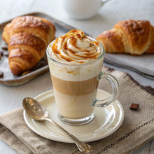 Vanilla caramel latte in clear glass cup with foam, spoon, and croissants on plate.