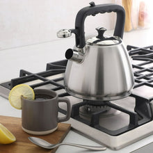 Stainless steel tea kettle with black handle and lid on a gas stovetop
