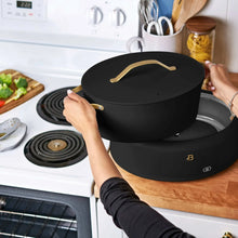 Black multi-cooker pot with lid and gold-tone handle rests on a stovetop