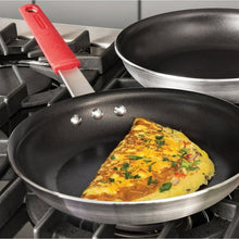 Nonstick small frying pan on a gas burner with a yellow omelet and red handle.