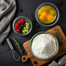 Glass mixing bowls with eggs, berries, and flour plus egg whisk