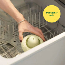 Mint green treat-dispensing dog toy being placed in a dishwasher-safe rack