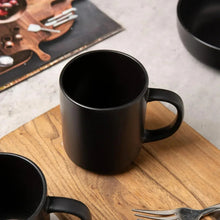 Black stoneware mug with curved handle, with bowl beside it