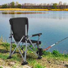 Black folding camping chair with mesh back, armrests, and cup holder on riverside.