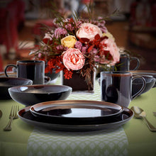 Black dinnerware set on table: plates and mugs with metallic accents