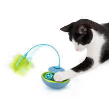 Electronic cat toy on floor with feather wand and ball, sniffed by a cat.