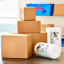 Large shipping box stack in brown cardboard with packing materials and label roll