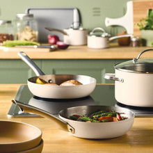 Stainless skillet and covered pots with white exteriors on a kitchen counter