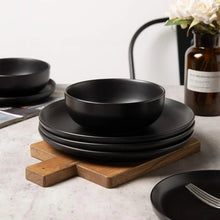 Black stoneware bowl and stack of matte plates on wooden risers