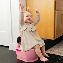 Pink toddler potty training seat with white top, black handles, and splash guard
