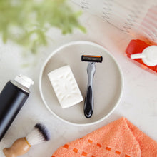Disposable 4-blade razor on sink with soap, brush, and orange towel