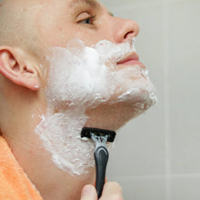 Men's face with white shaving foam and a disposable 4-blade razor