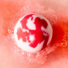 Bath bomb dissolving in water with red and white foamy bubbles