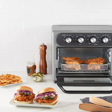 Air fryer oven with open basket holding roasted food, four control knobs