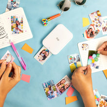 White mini photo printer on desk with small photo prints being handled