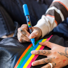 Hand holding a blue POSCA marker coloring a brightly colored fabric