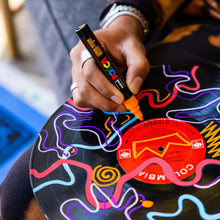 Hand coloring a circular template with an orange POSCA marker tip