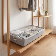 Gray under-bed rolling storage bin under a wooden bench holding folded towels and clothes