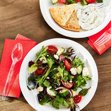 Clear plastic fork and spoon on salad plate at a table