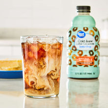 Cold brew coffee concentrate bottle with donut label beside glass of iced coffee