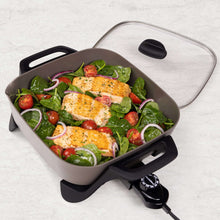 Ceramic electric skillet with glass lid containing chicken over spinach and tomatoes