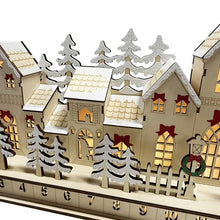 Close-up of wooden Advent calendar village showing snowy trees, house windows, and numbered drawers