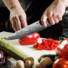 Hands using a Damascus chef knife with black resin handle to chop vegetables