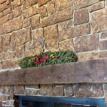 Fresh mantel garland across fireplace ledge with green pine and red blooms