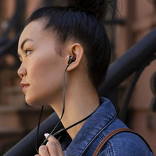 Wireless in-ear earphones worn by a person with black earbuds and blue jacket