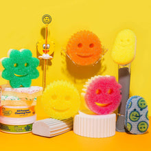 Assorted smile-shaped cleaning sponges on a display, including yellow and pink scrub faces