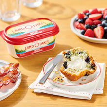 Butter tub with canola oil beside toast, butter knife with spread, berries plate
