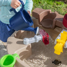 Pump and Splash water table with child pouring water into the beige basin and red pump.