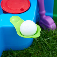 Plastic scoop seat holding white ball on green base beside blue tub and purple pipe