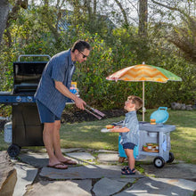 Blue children’s BBQ play cart with umbrella, toy utensils, and toy food in side bins