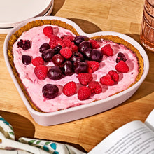 Heart-shaped stoneware baking dish with pink cream and mixed berries