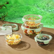 Four round glass food containers with green lids and floral print, on wooden table