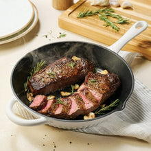 White enameled cast iron skillet with cooked meat, black interior and long handle