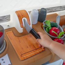 Toy sink area with wooden cutting board, toy knife, and pretend vegetables