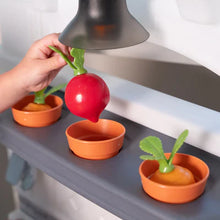 Toy play kitchen counter with orange cups and red and green vegetable props